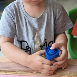 Child screws blow plastic bolt nut on blue plastic screw in class during one of The Garden's Montessori workshops in their bilingual school in Paris.