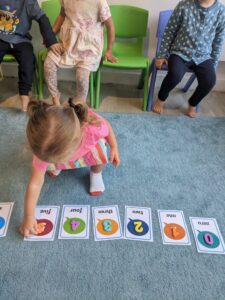 Young student matches different colored plastic numbers to a sheet with the wor written out in English on the floor in class during one of The Garden's workshops in their bilingual school in Paris.